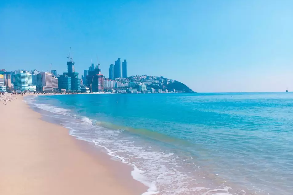 2023年9月釜山海灘景觀，藍天和波光粼粼的海水，左側遠處高樓林立，展現韓國釜山秋季的晴朗氣候。