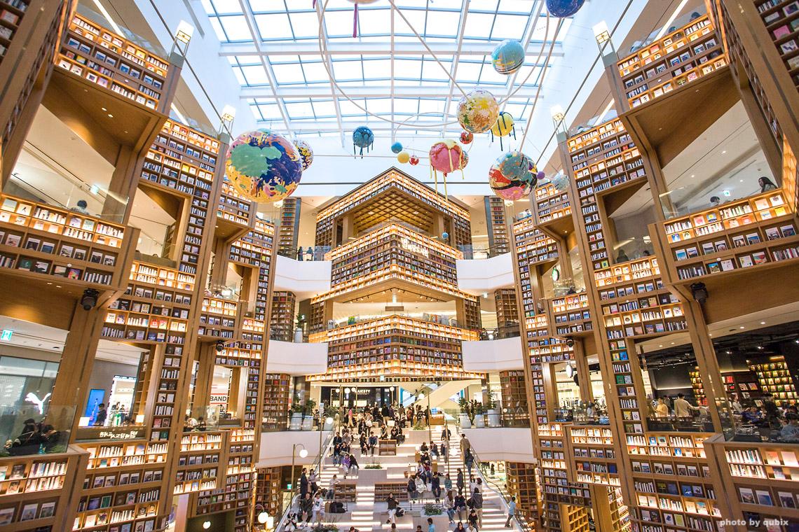 首尔三成COEX星空图书馆内景,书架高耸,两侧悬挂有色彩斑斓的地球模型装饰。人群在图书馆内漫步。