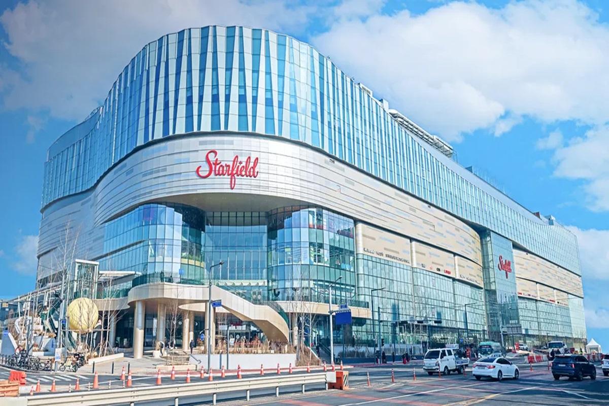 韩国Starfield购物中心外观,现代建筑设计,蓝色玻璃墙外立面,购物中心标志明显可见。车流环绕建筑周围。