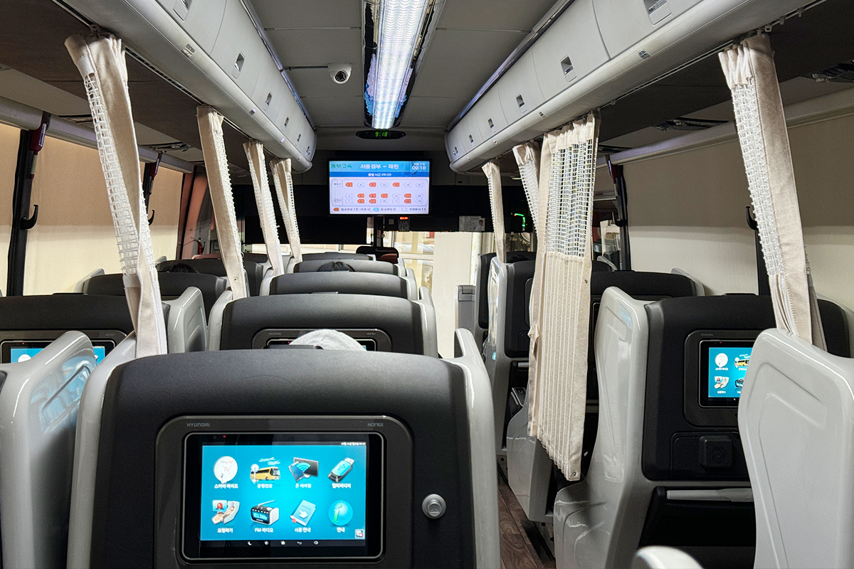 Interior view of a premium bus with individual screens and spacious seating, reminiscent of business class.