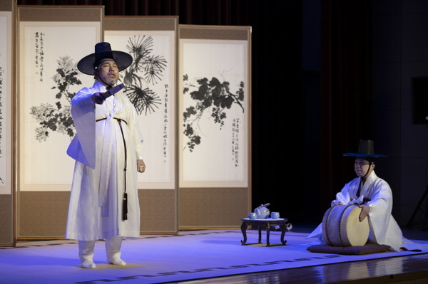 演员在舞台上演出盘索里，穿着传统韩服，在屏风前操作鼓。