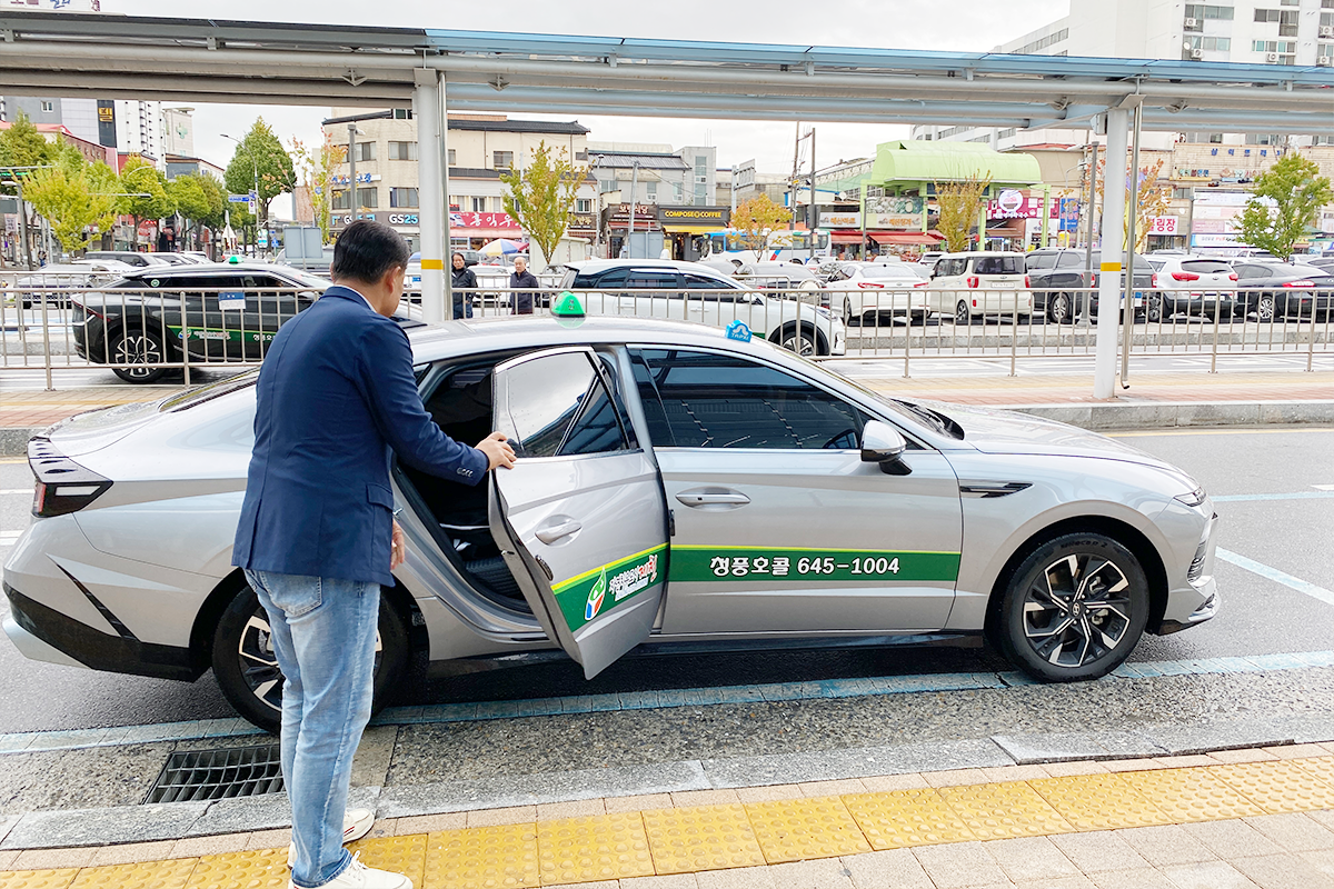 Private taxi tour service in Jecheon with driver assisting a passenger into a sleek vehicle
