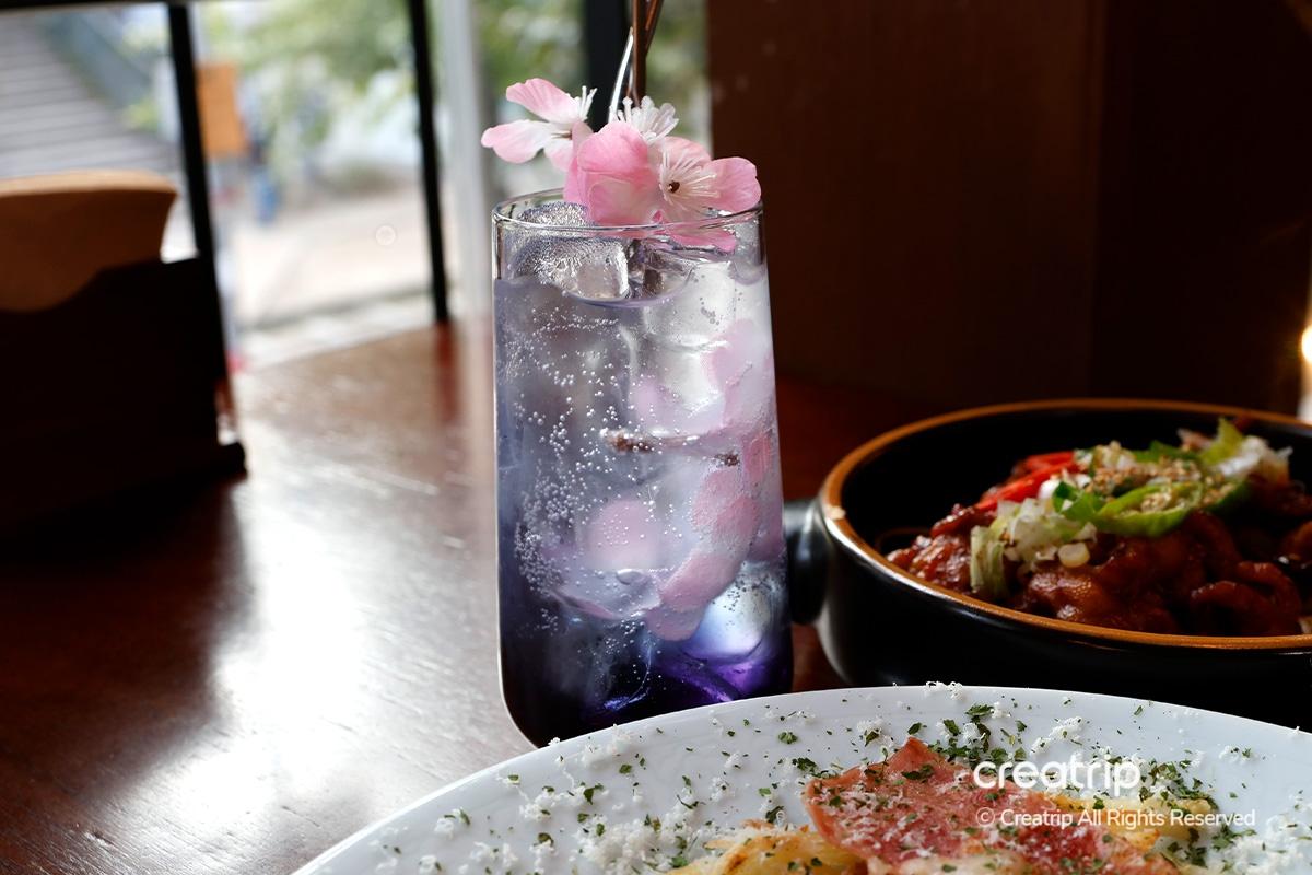 Elegant purple cocktail at Earl topped with flower blossoms, alongside spicy chicken dish.