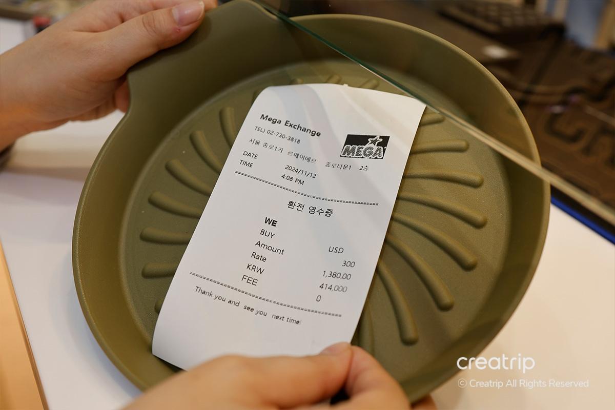 Ricevuta di cambio valuta visualizzata su un vassoio presso il Mega Currency Exchange, documentando i dettagli della transazione.