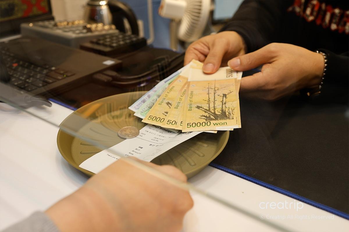 Il membro del personale al Mega Currency Exchange restituisce won coreani al cliente come risultato dello scambio di valuta.