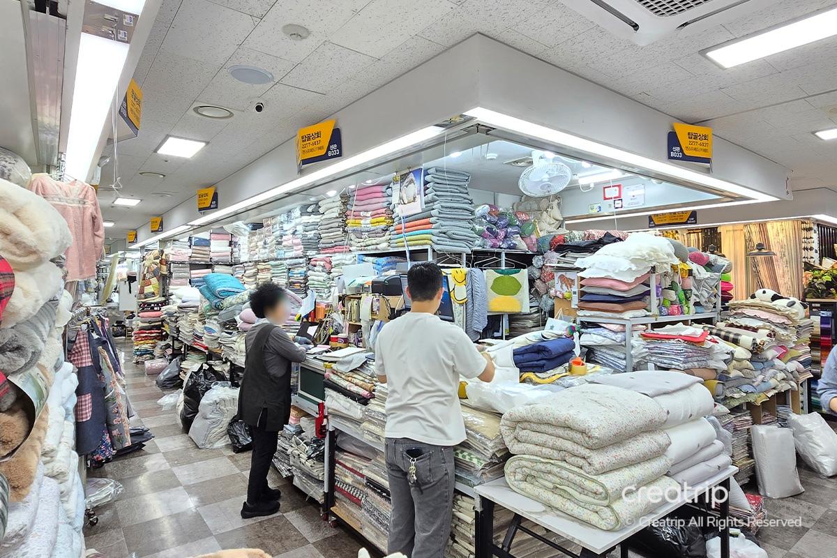 塔洞商會專賣店的室內場景，售賣多款花紋多樣的牀上用品，店內佈置整潔，牀墊和被子堆放整齊。