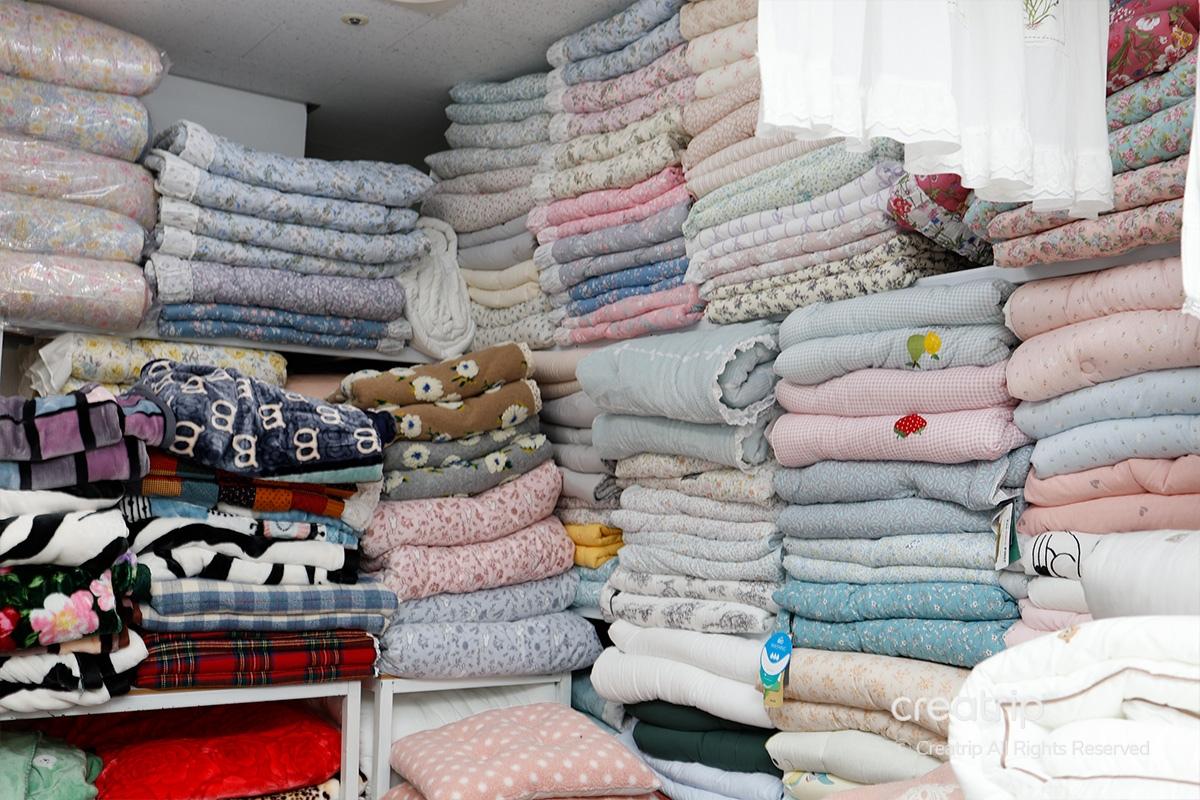 被子陳列貨架，呈色彩柔和的粉色和淺紫色系，以及多個印花圖案的牀具用品，排列緊湊。