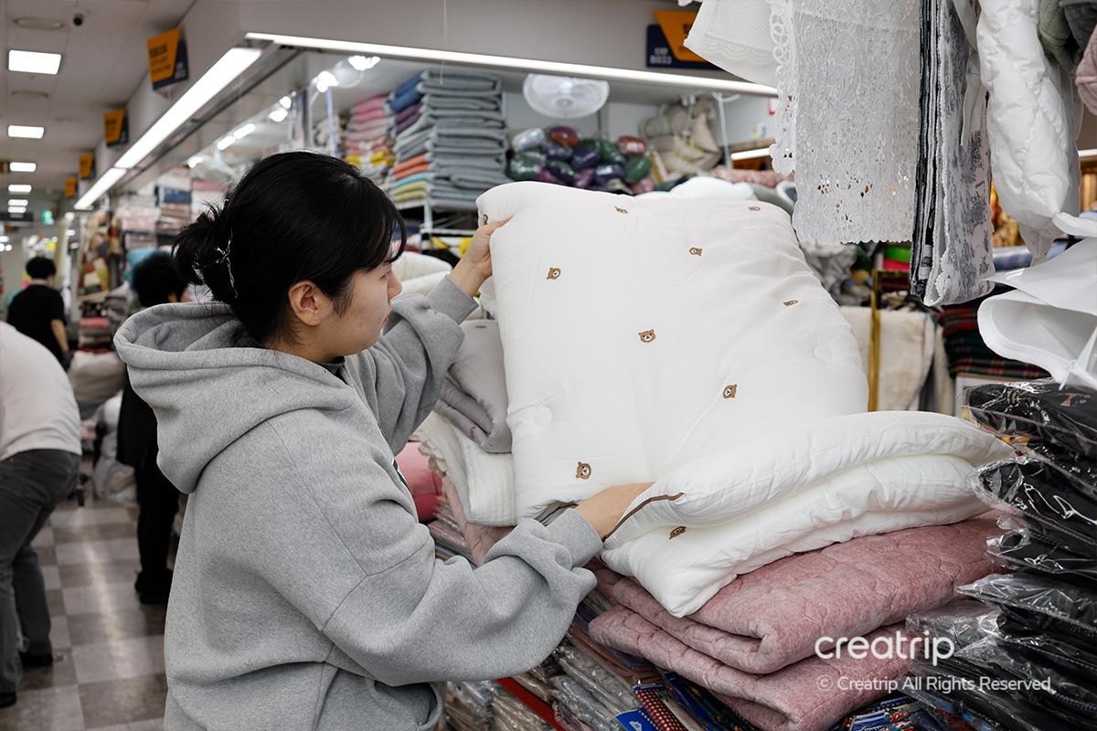 女子在塔洞商會店內觀看白色熊圖案被子，展現被子的柔軟面料和可愛設計，目標顧客是重視舒適感和設計的消費者。
