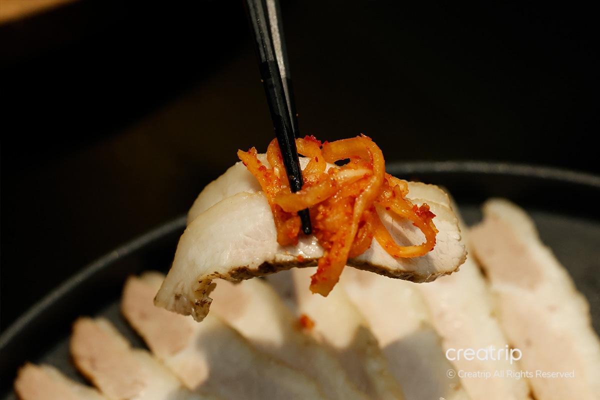 Bocado de cerdo y rábano fresco tomado con palillos en JINJAK KAKII.