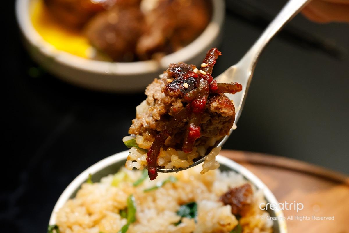 Tenaza sujeta un bocado de Tteokgalbi con arroz en JINJAK KAKII.