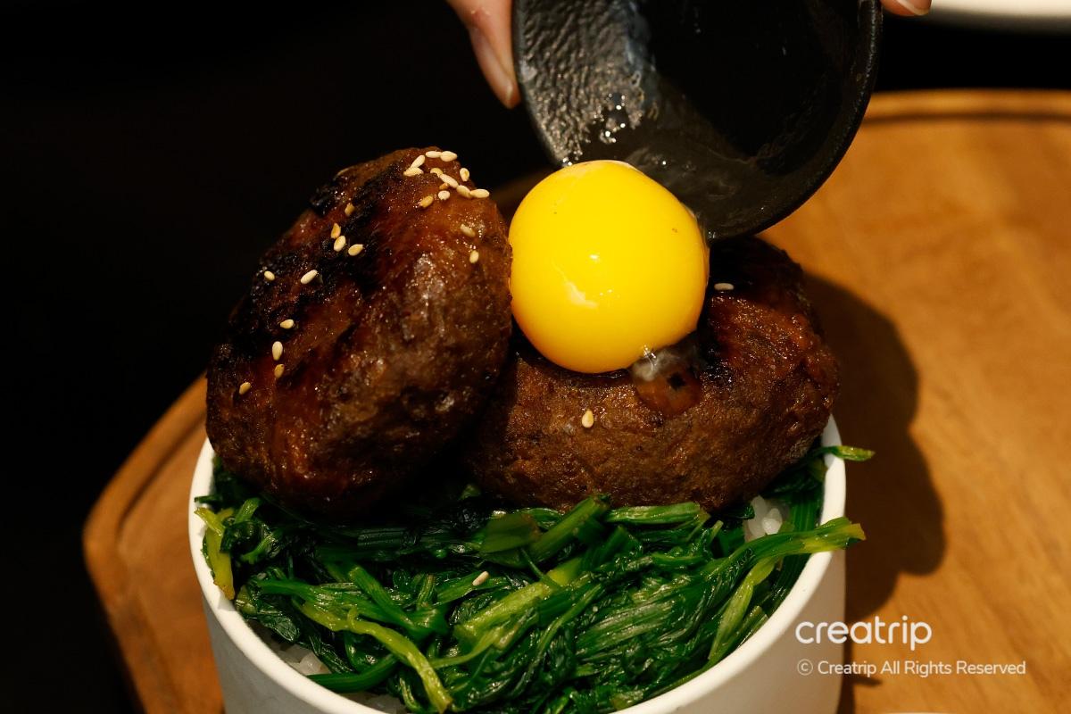 Tteokgalbi cubierto con yema de huevo en un tazón de arroz en JINJAK KAKII.