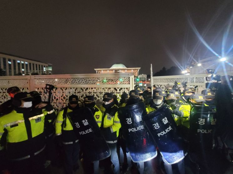 韩国警察在国会前部署，阻止议员进入国会议事堂。照片中可见警察穿着防暴装备，场景为夜晚。