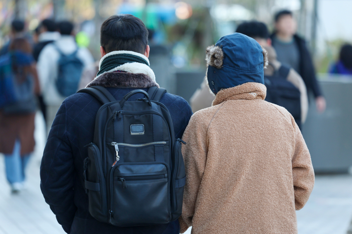 Two individuals walking on a Seoul street in winter coats, showcasing the chilly February weather in South Korea.