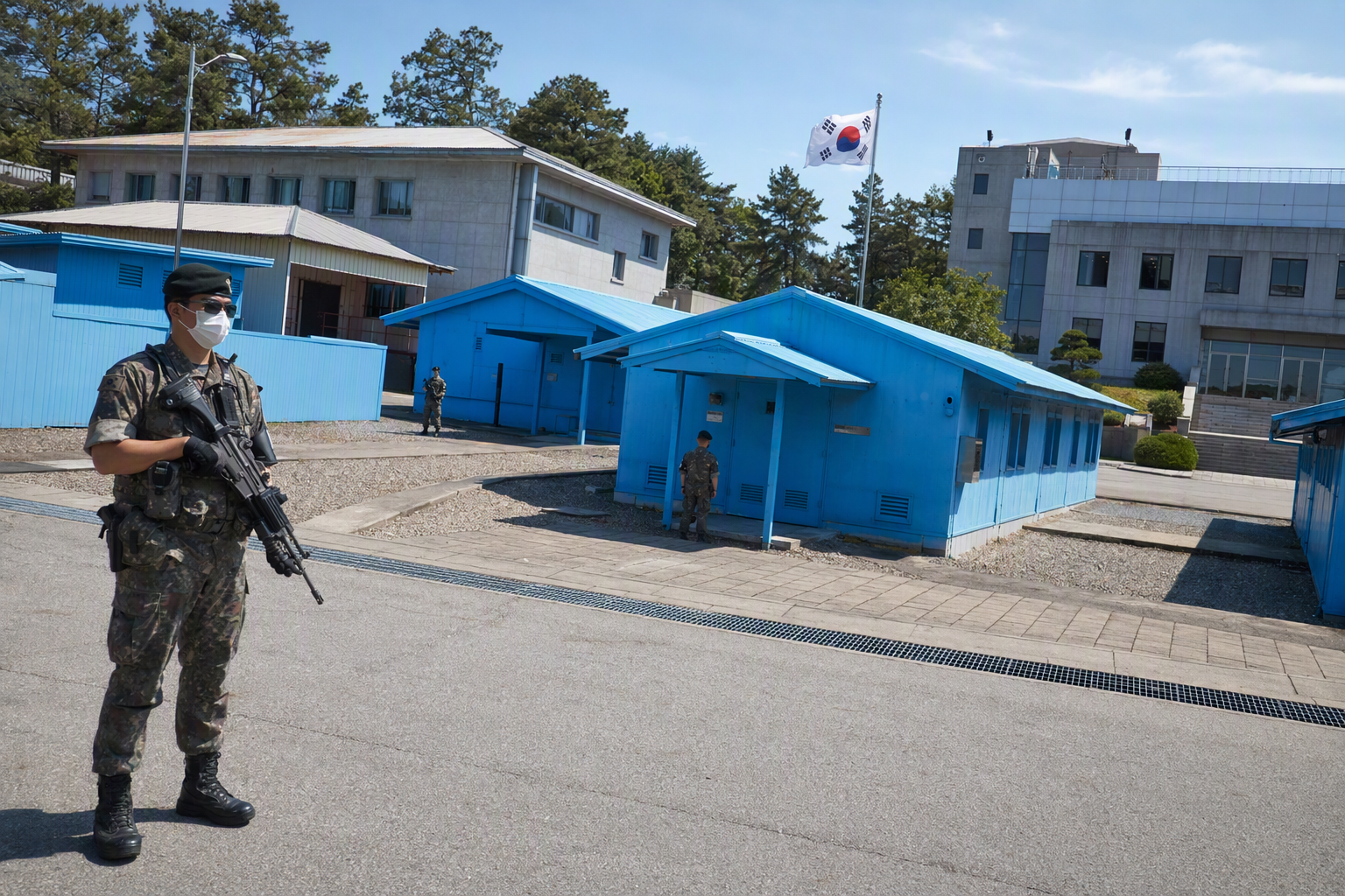 Photorealistic view of Panmunjom blue conference buildings from the South Korean side, soldiers standing guard, bright sky, crisp details, no Korean text