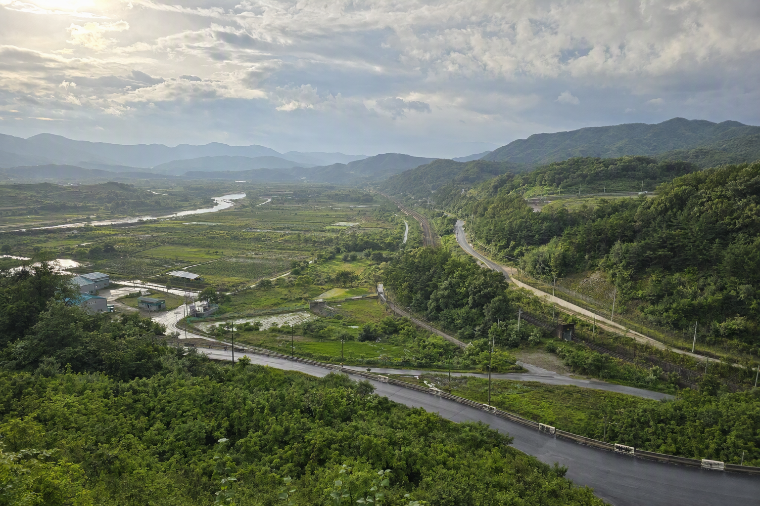 Photorealistic aerial-style view of the Korean DMZ landscape, layered green hills, fence lines, wide buffer zone, soft sunlight, vivid natural colors, no Korean