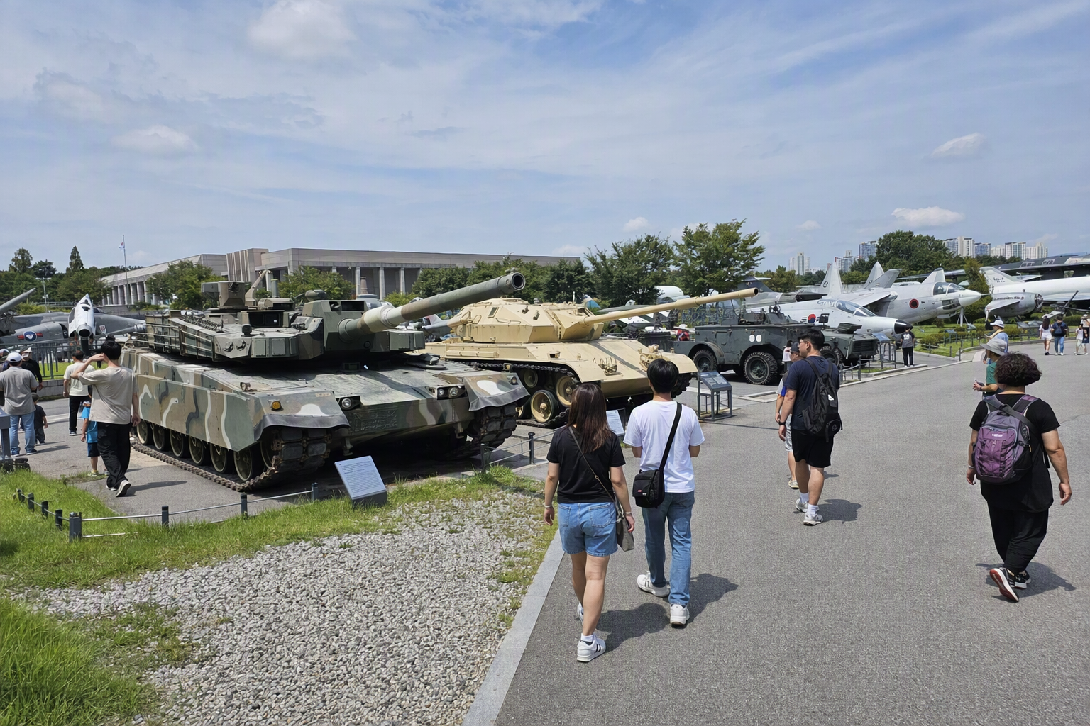 Bright photorealistic outdoor military display with tanks and aircraft, expansive museum grounds, vivid daylight, families exploring, no Korean text