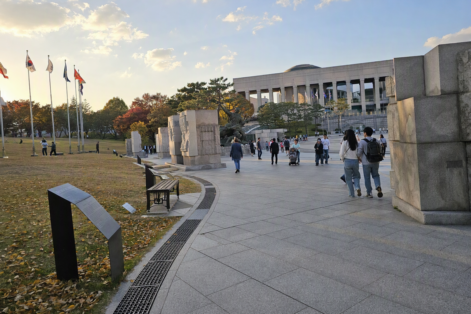 Bright photorealistic wide museum grounds in late afternoon, visitors walking between exhibits, calm sky, spacious memorial atmosphere, no Korean text