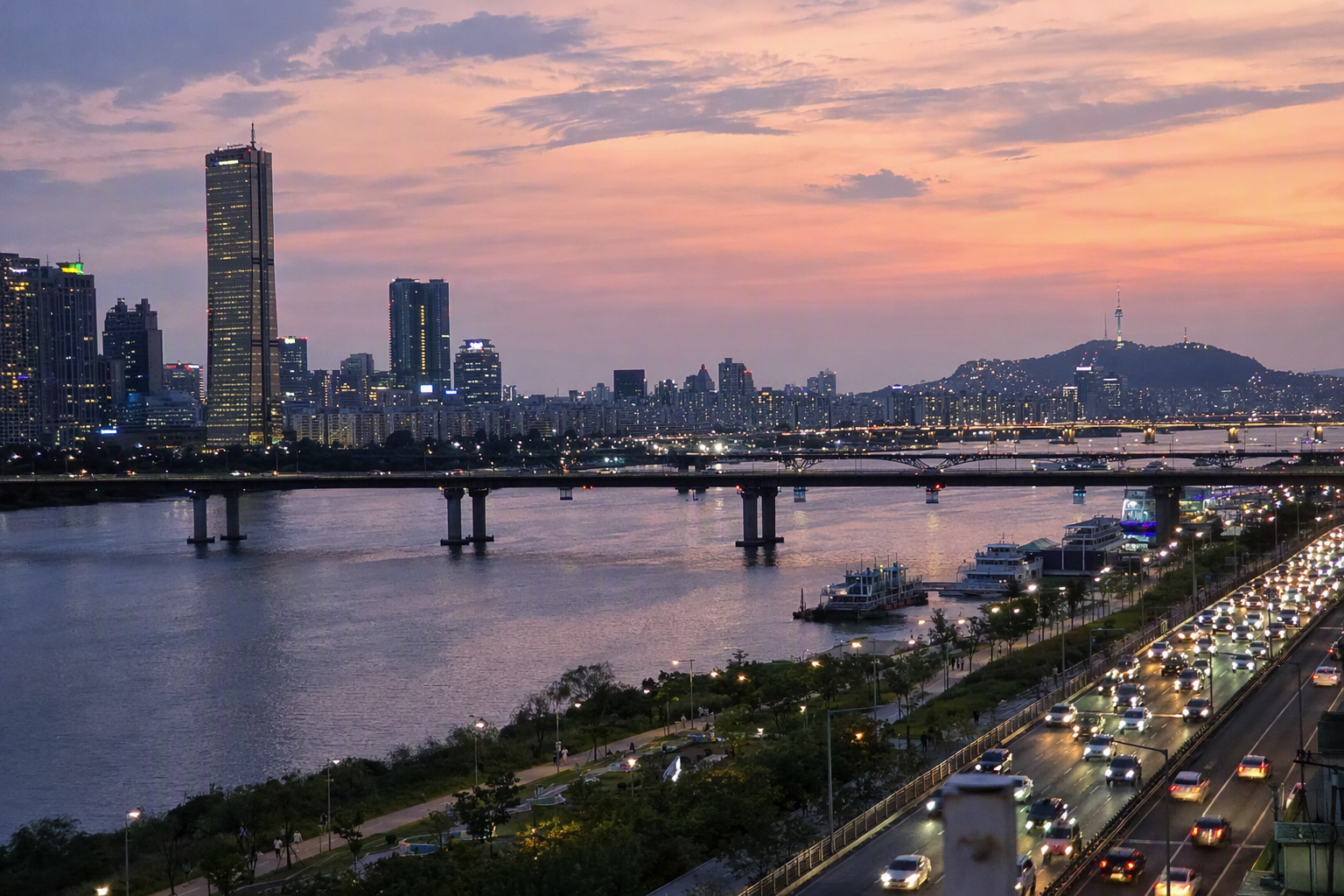 Bright, vibrant, photorealistic Seoul skyline at sunset, Han River reflecting city lights, modern towers under a warm pink sky, editorial travel mood, no Korean