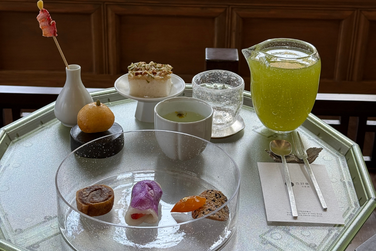 韓屋窗邊的1人份宮廷茶果套餐：玻璃盤盛多款傳統點心、圓杯金菊迎賓茶及綠色茶壺，器皿精緻、擺盤典雅，呈現古好齋季節茶點與韓屋靜謐氛圍。