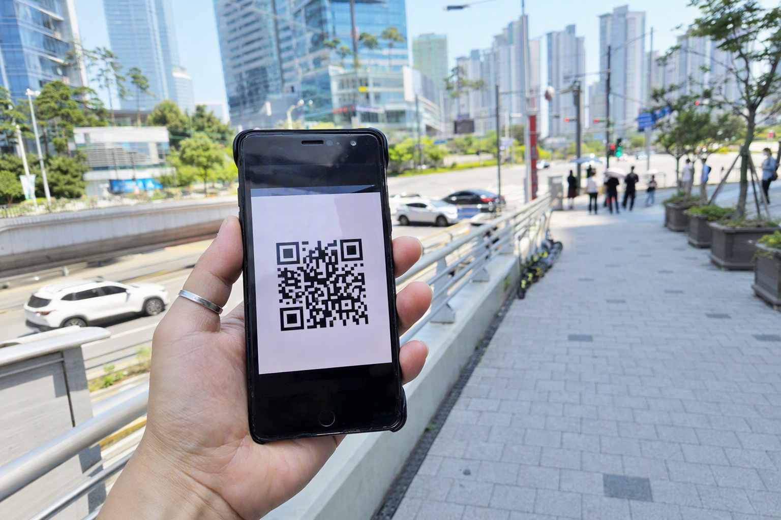 Photorealistic close-up of a hand holding a smartphone showing a QR code pass, cityscape background, bright daylight, no text