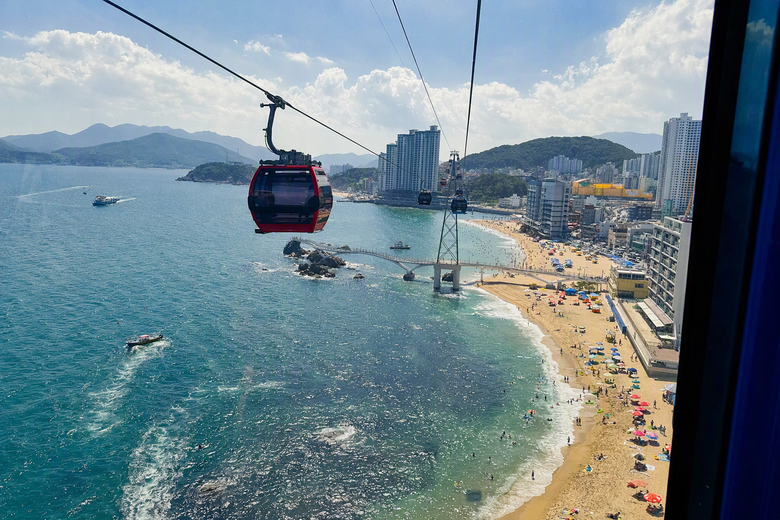 Bright vibrant photorealistic Songdo sea cable car over blue ocean in Busan with coastline, small beach, sunny sky, travel photography style, no text