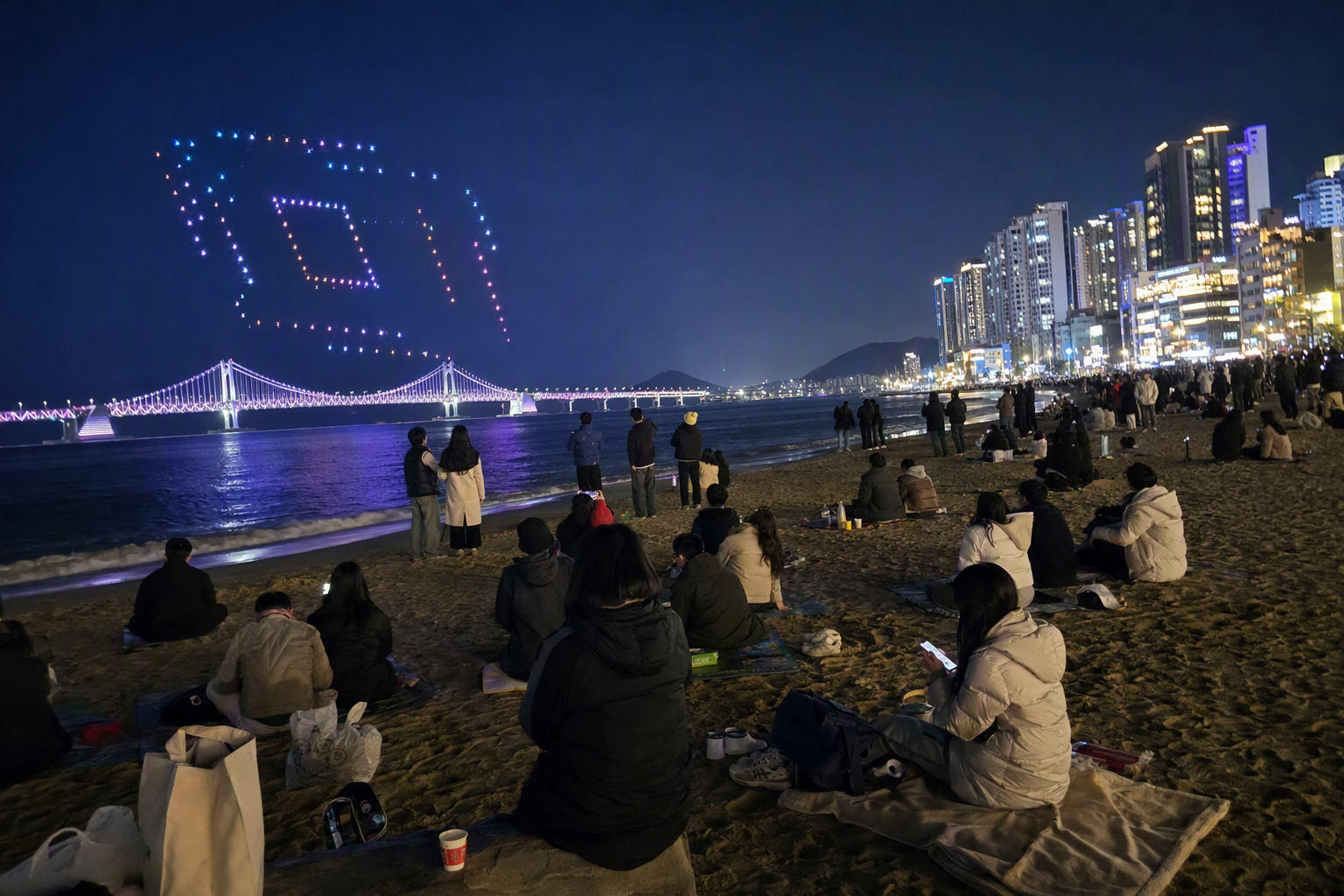 Bright vibrant photorealistic night scene at Gwangalli Beach with illuminated Gwangan Bridge, colorful drone lights in the sky, people watching from the sand, n