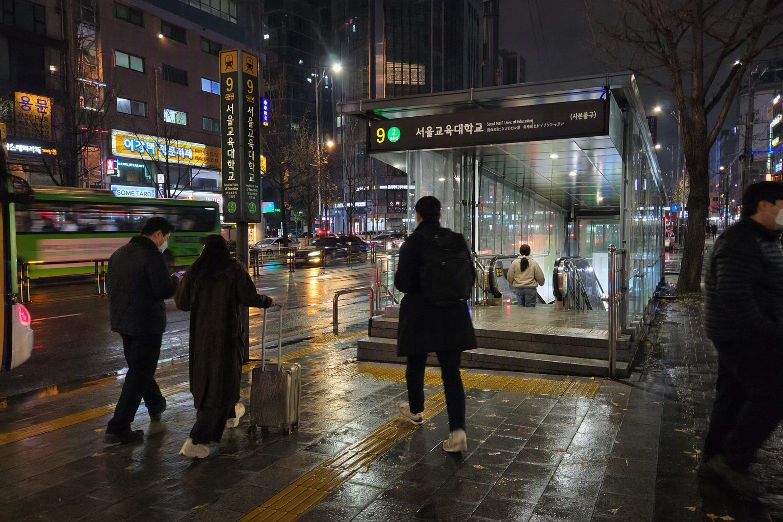 首爾地鐵出口外明亮寫實的夜景,有城市燈光與旅客,氛圍乾淨現代,沒有可辨識文字