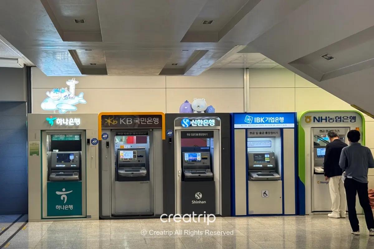 濟州機場一排銀行自動提款機與換錢櫃位，包含多家韓國銀行標誌與顧客排隊使用，顯示機場1樓抵達層可即時提領現金的便利設施。