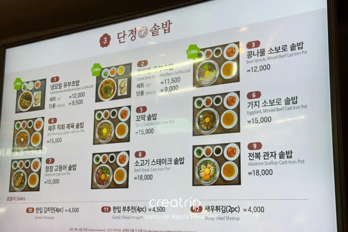 濟州機場美食街電子菜單板：九款定食照片與價格（石鍋拌飯、鮑魚、牛排等），下方列有小菜、煎餅和炸蝦等配菜選項，適合準備登機前用餐參考。
