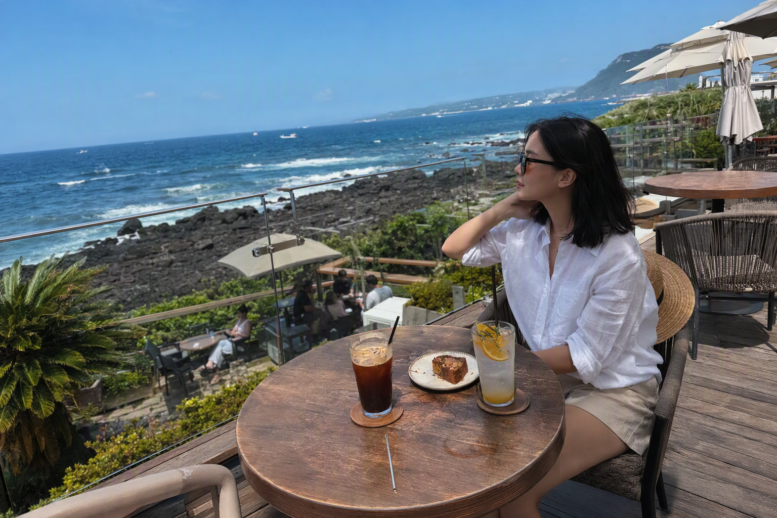 Bright photorealistic cafe terrace in Aewol Jeju overlooking blue ocean waves, iced drinks on a table, soft sunlight, modern coastal atmosphere, no text