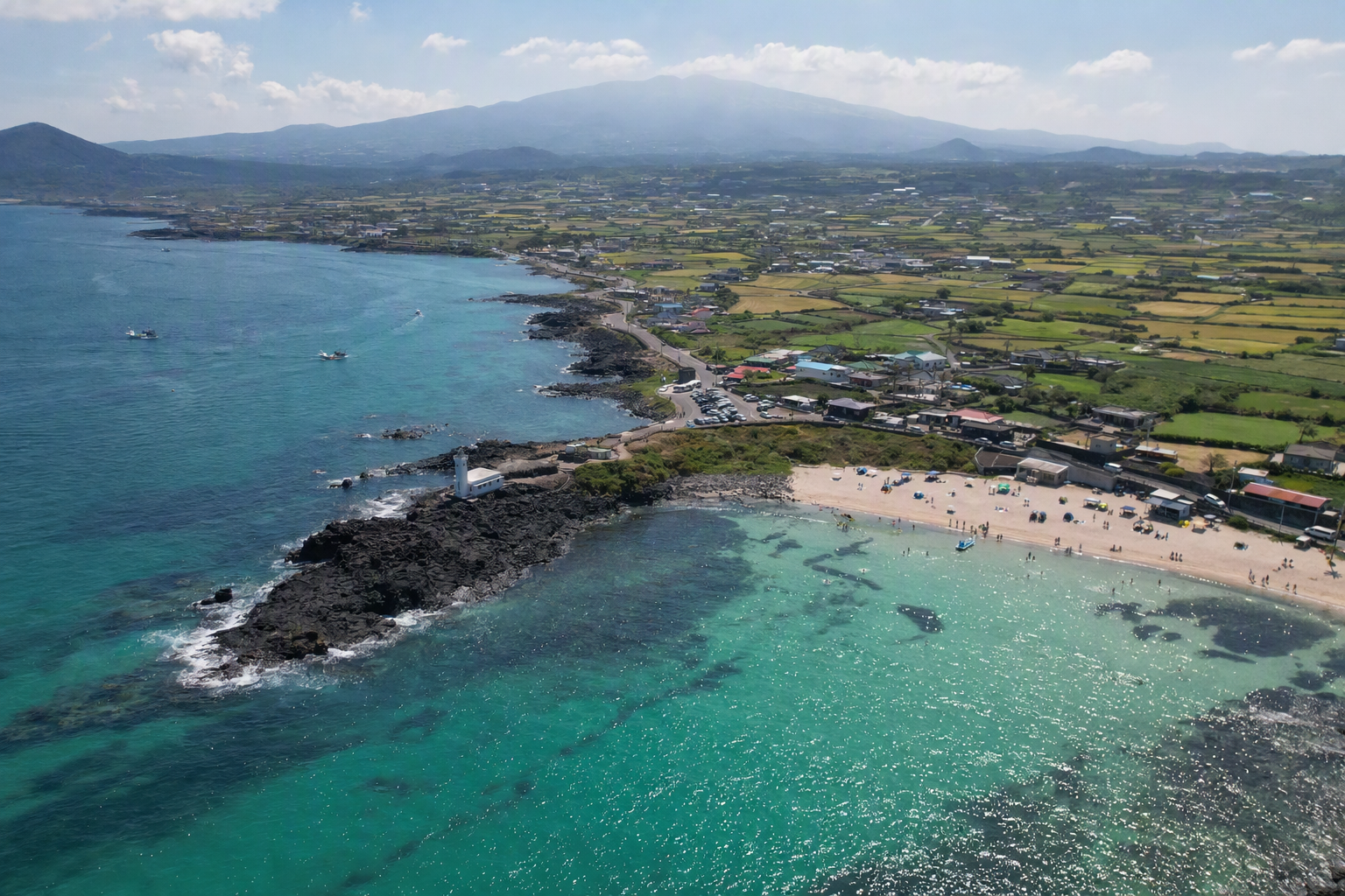 Bright photorealistic aerial view of Jeju Island coastline with turquoise water, black volcanic rocks, green fields, and a clear blue sky, no text