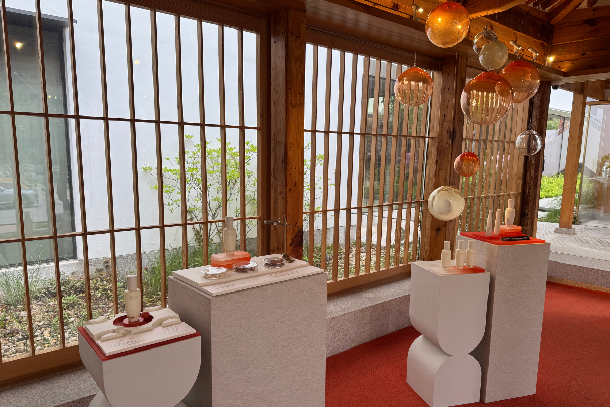Sulwhasoo Bukchon House interior display with traditional wooden lattice windows, stone display tables, skincare products, and orange-themed decor.