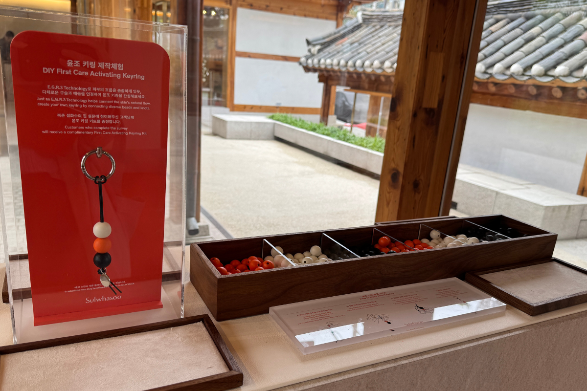 Sulwhasoo Bukchon House DIY area with red, white, and black beads in wooden boxes, display cards, and a view of traditional hanok roof tiles and the courtyard outside.