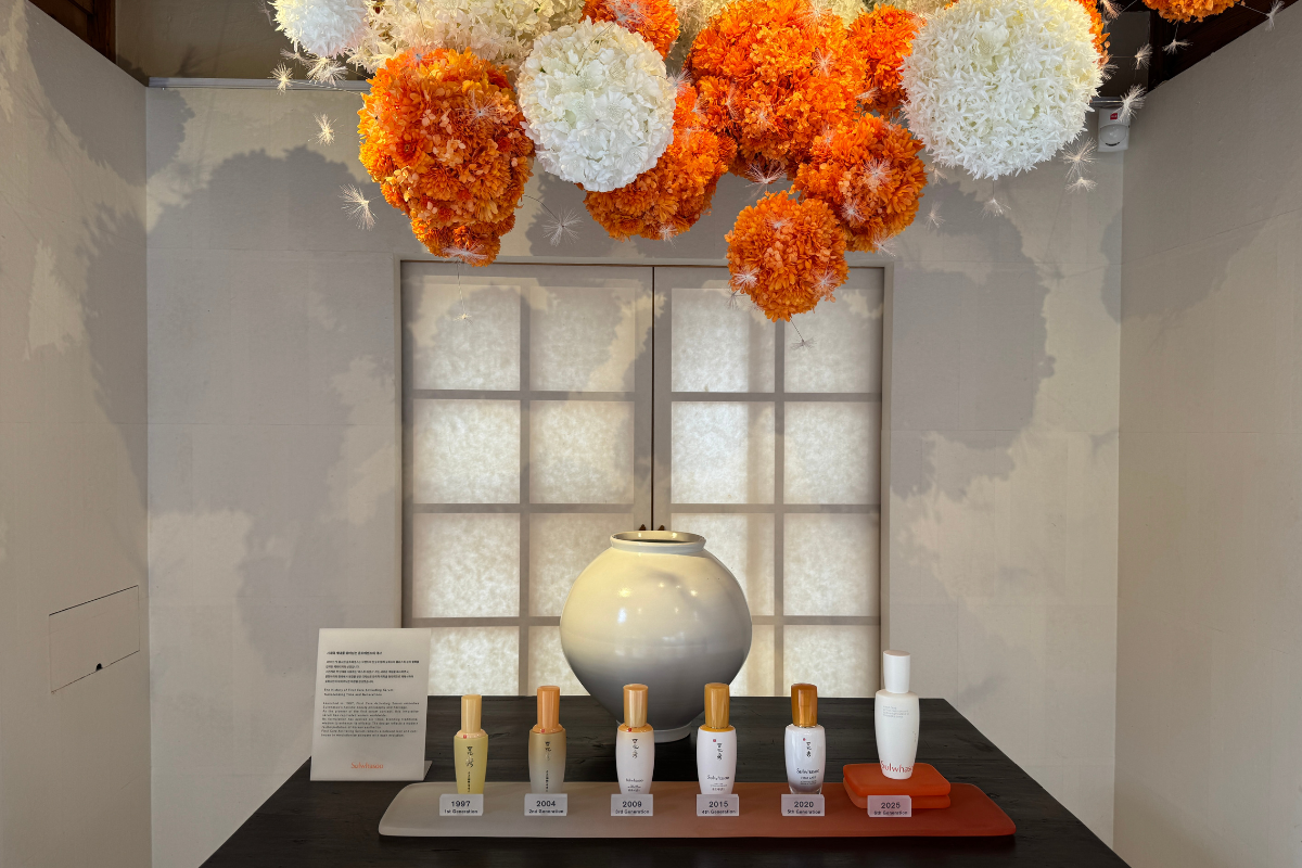 Sulwhasoo Bukchon House display featuring skincare bottles, a large ceramic jar, backlit paper windows, and orange-and-white hanging flower decorations.