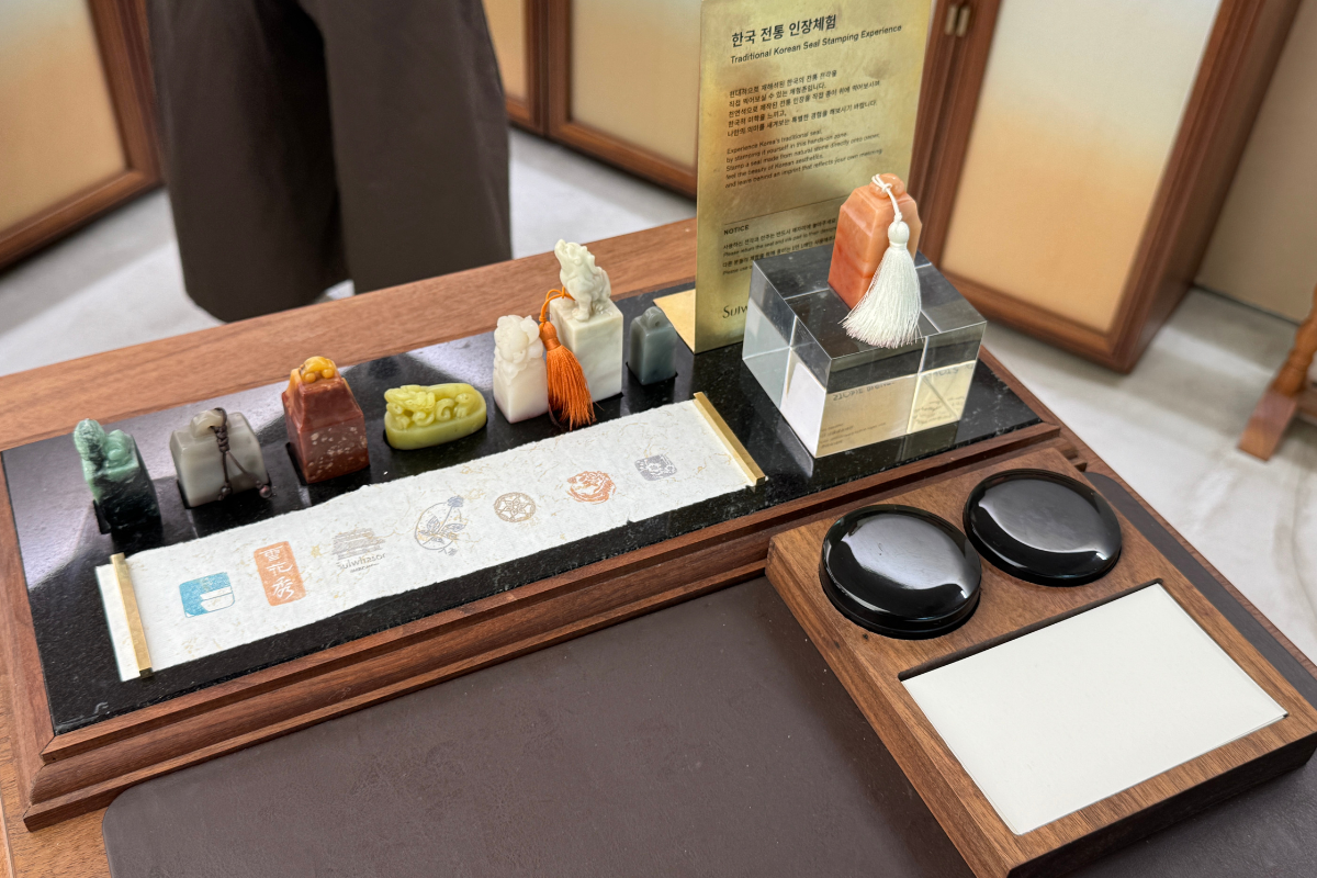Khu vực tự làm con dấu nhân sâm tại Sulwhasoo Bukchon House với con dấu đá và ngọc bày trên khay gỗ, cùng với miếng mực và mẫu tranh con dấu.