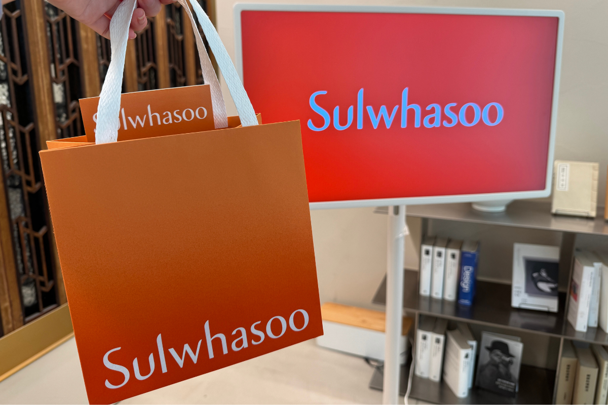Sulwhasoo Bukchon House shopping bag and brand sign, with an orange gift bag and white ribbon displayed inside the store.