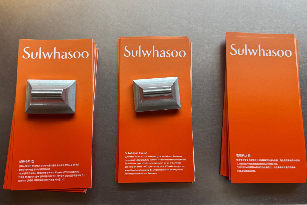 Three stacked orange Sulwhasoo brand cards with metal display weights, arranged on a brushed metal surface highlighting flagship store design.