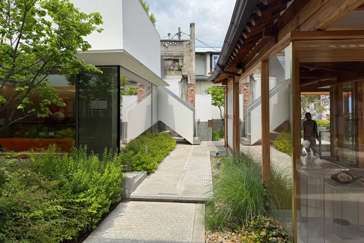 Courtyard at Sulwhasoo Bukchon House connecting preserved hanok wooden structures with a modern white building, stone paths, greenery, and stairs.