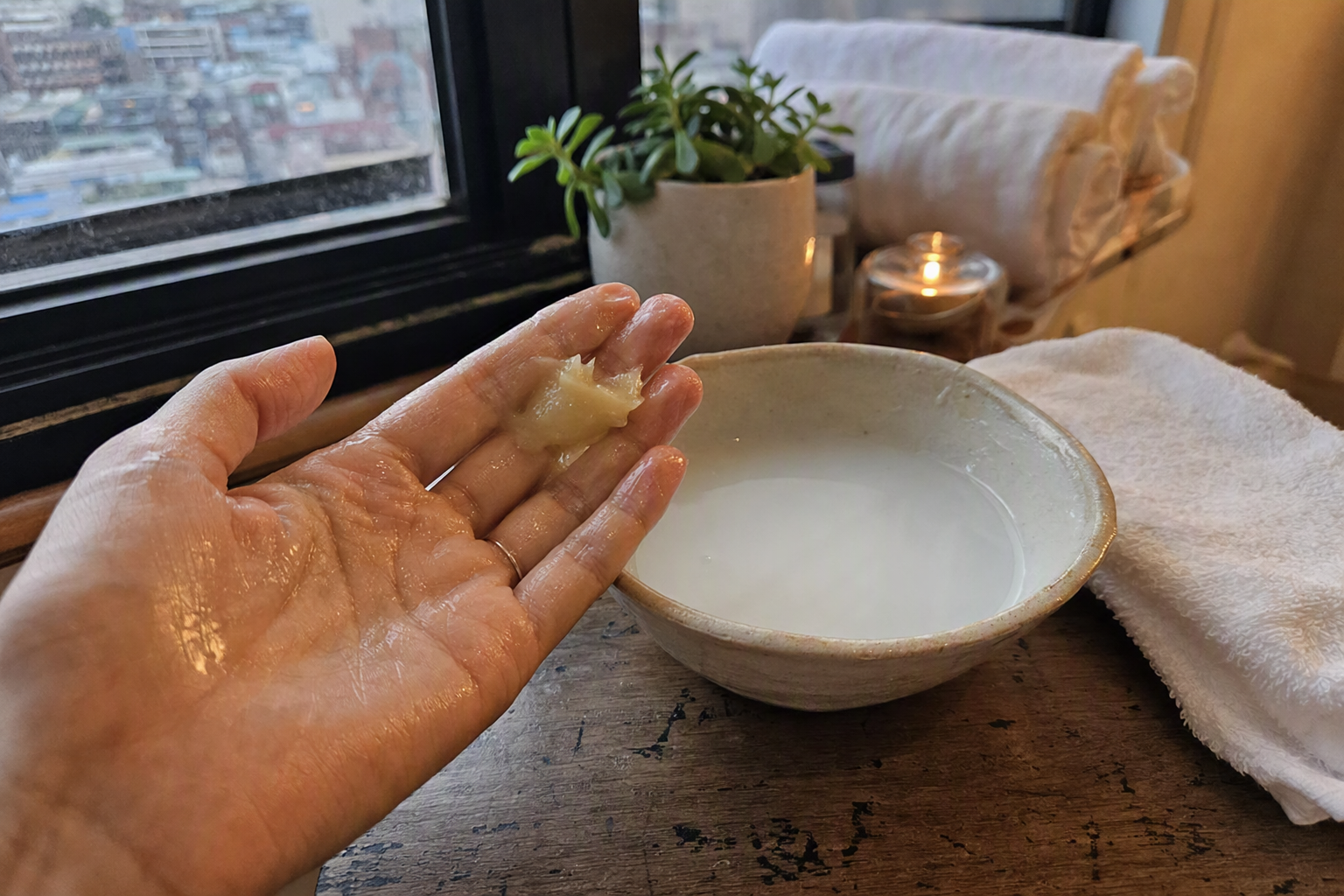 bright vibrant photorealistic close-up of cleansing balm melting on fingertips beside a small bowl of water and white towel, soft spa lighting, no visible label