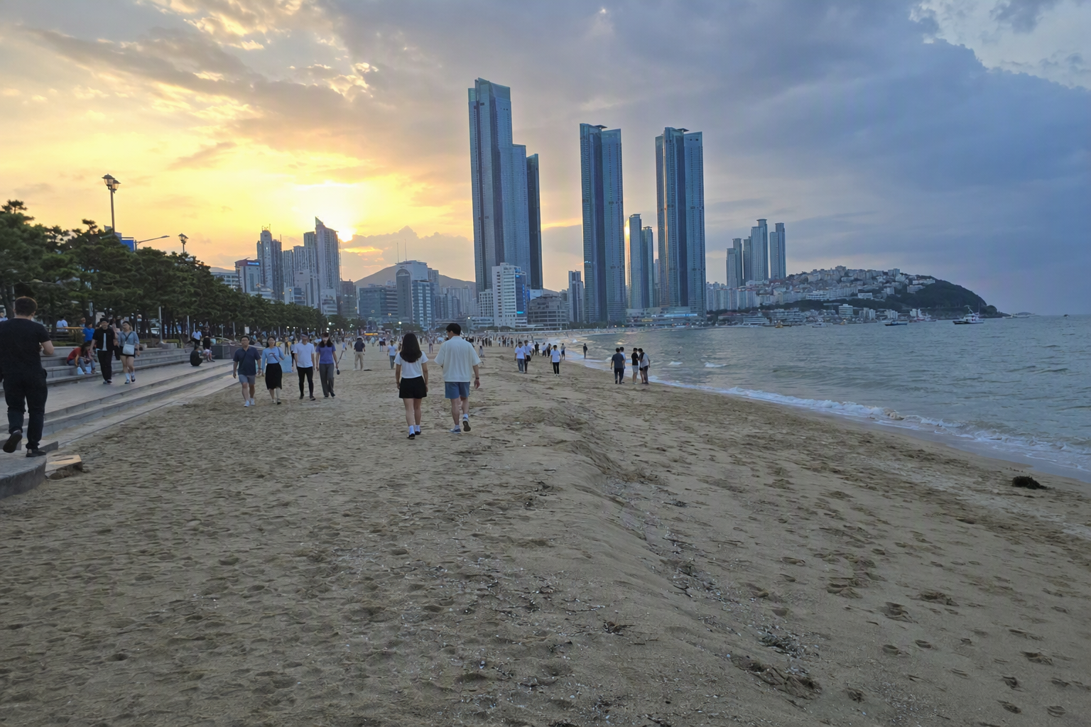 黃昏金色時段、海浪平靜，旅客散步嘅釜山海灘天際線，色彩明亮寫實，現代建築，畫面無可見文字