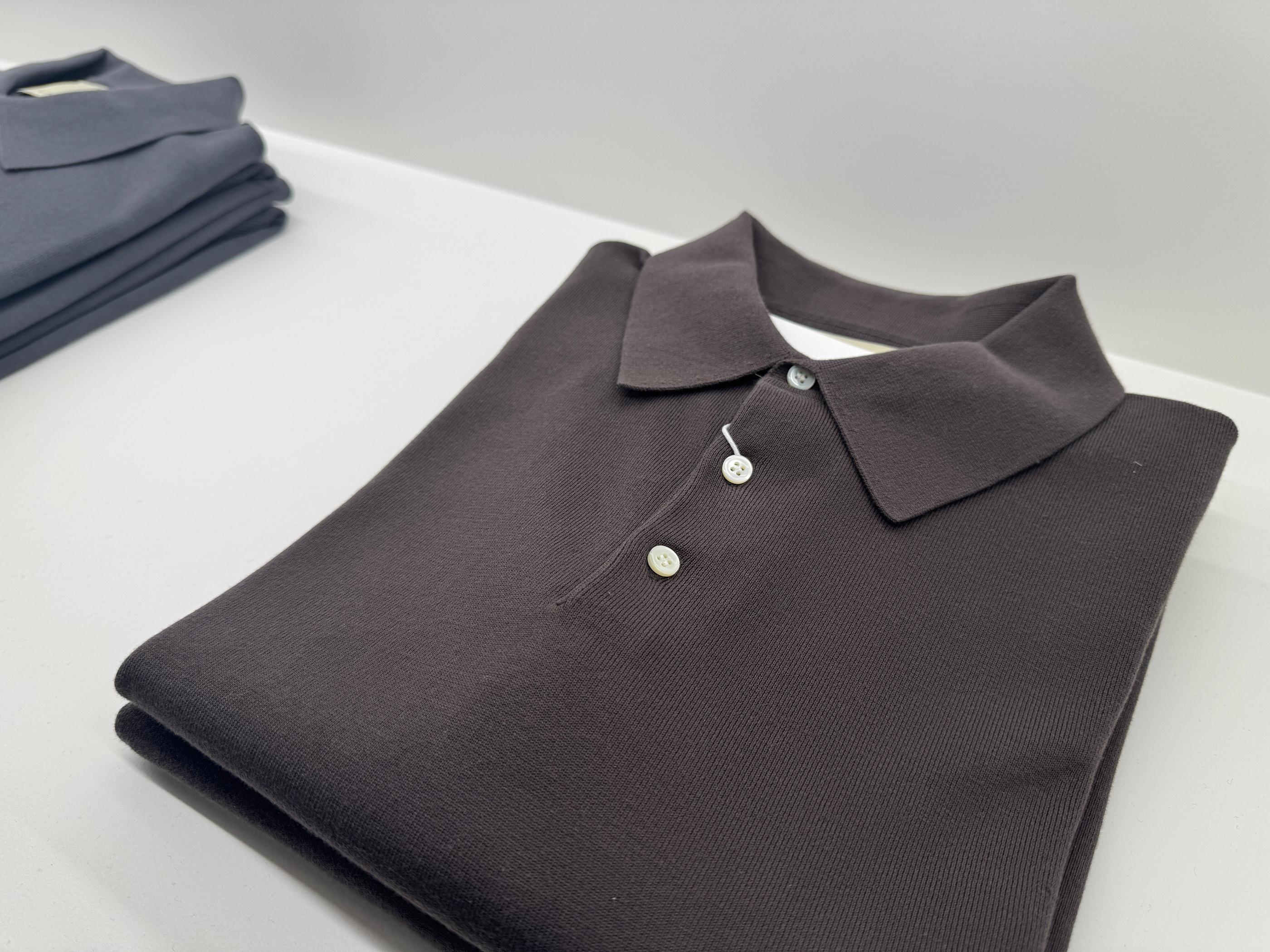 Minimalist dark brown knit polo neatly folded on a white display table inside Pottery Seongsu store, highlighting clean collar, button details and premium Korean menswear styling.