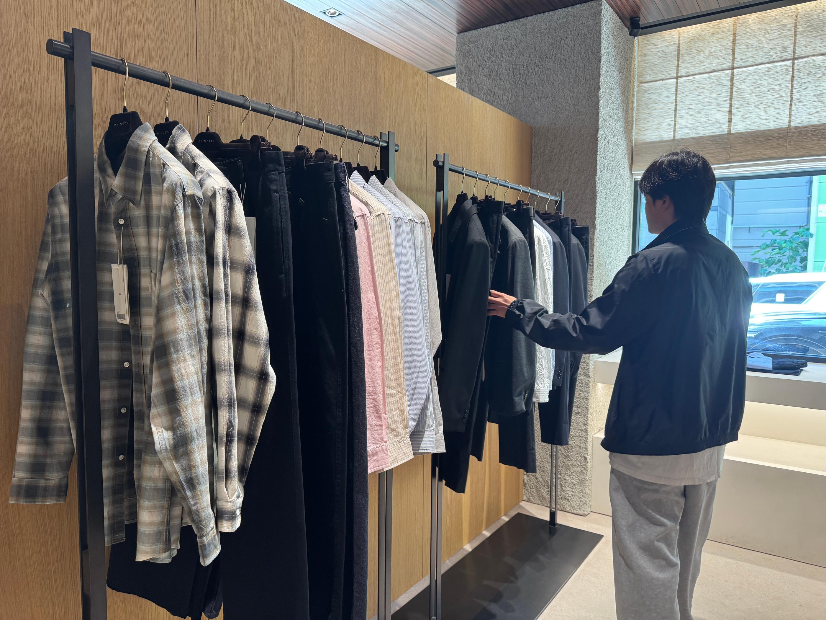Pottery Seongsu storefront display with cream polo shirts, logo caps and light-toned garments showcased on an illuminated shelf unit