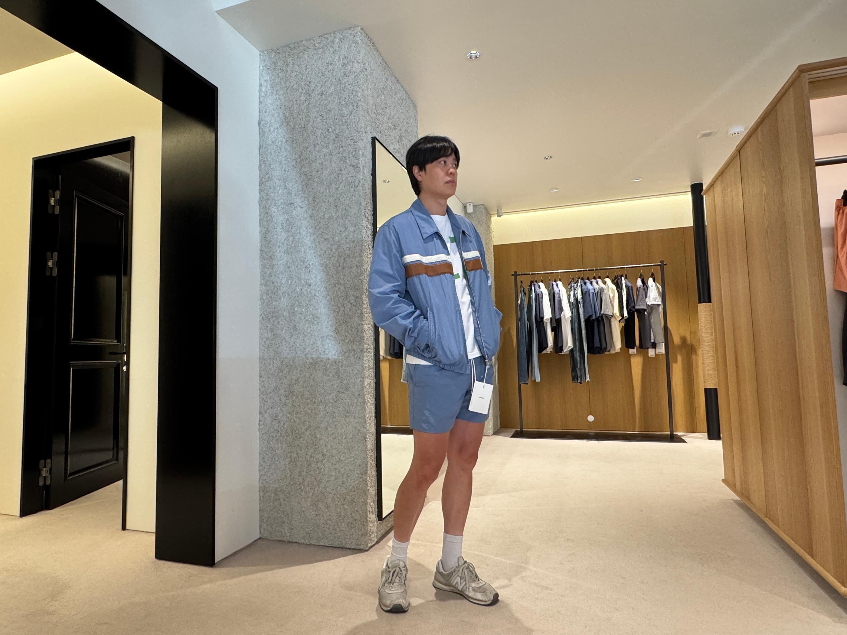 Male shopper modeling a sky-blue matching jacket and shorts set with white tee and sneakers inside Pottery Seongsu store, minimalist wooden racks and fitting rooms in the background