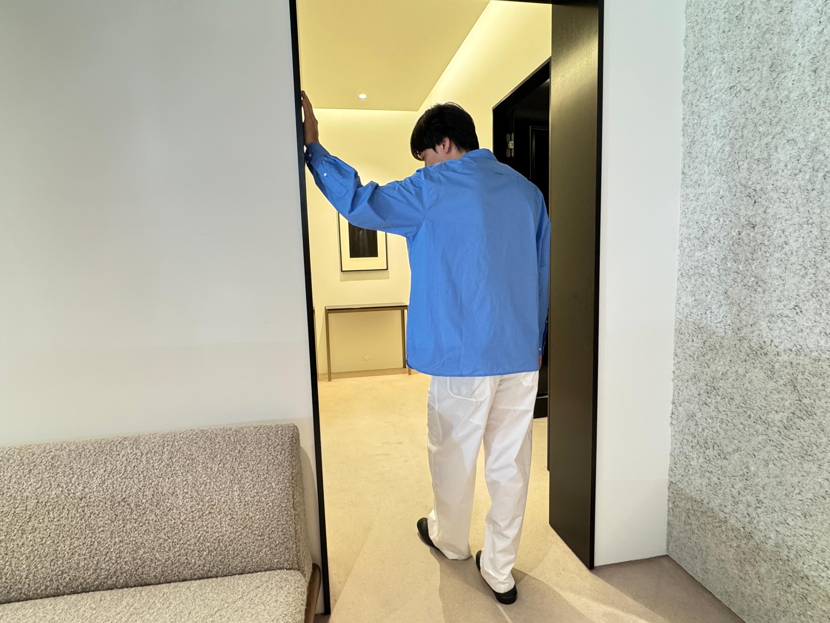 Male model seen from behind in a Seongsu Pottery fitting room wearing a sky-blue oversized shirt and off-white wide-leg pants, demonstrating the brand’s relaxed, minimal summer silhouette.
