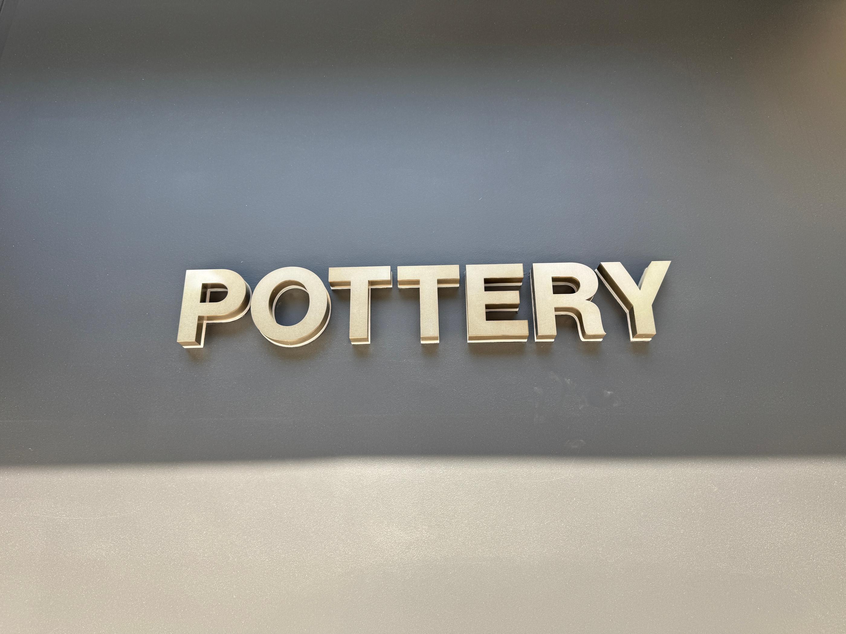 Front view of Pottery display wall featuring layered polo shirts in soft pastels, branded caps and seasonal knitwear on wooden shelves