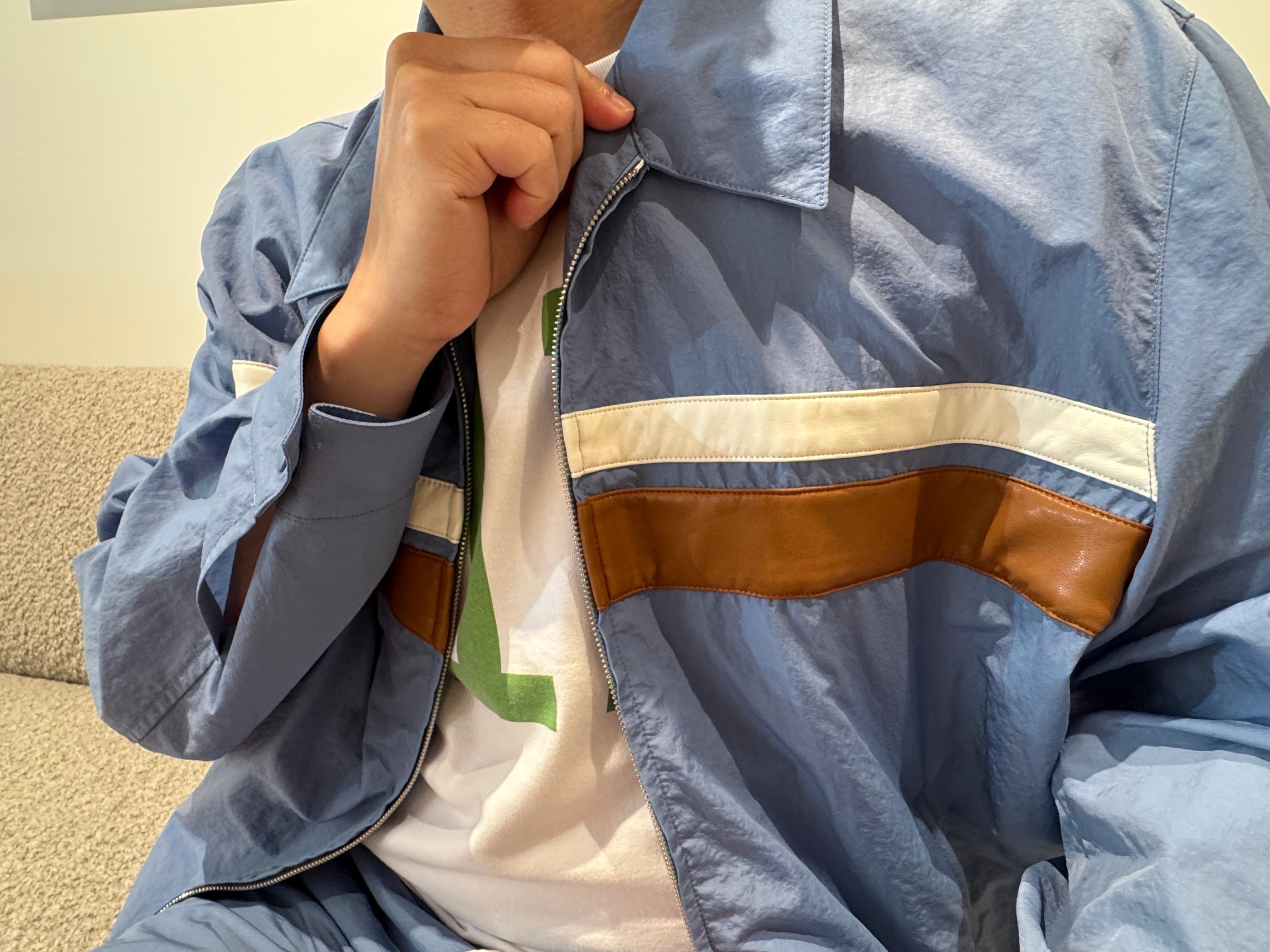 Model wearing Pottery sky-blue zip jacket with cream and brown color-block stripe over a white tee, seated in the Seongsu store fitting area