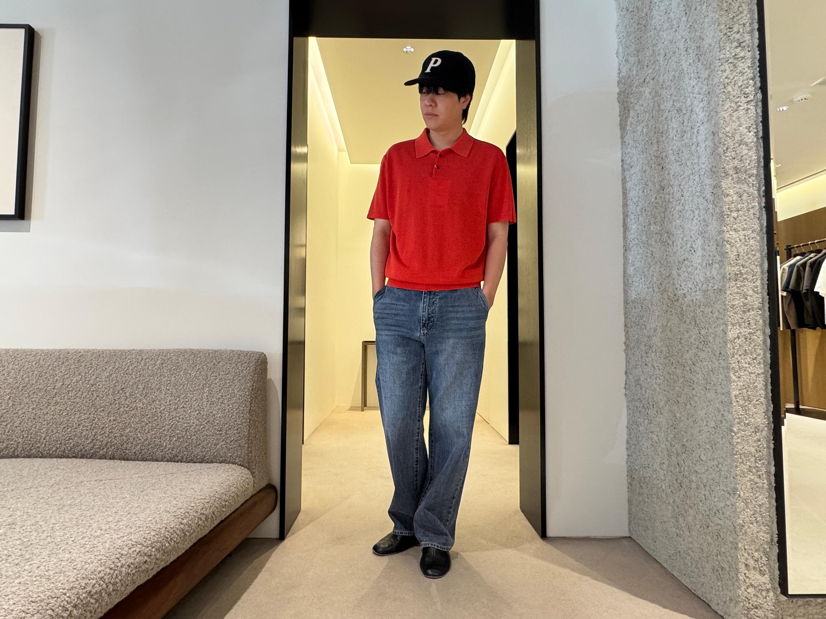 Model in a Pottery store doorway wearing a brick-red knit polo, relaxed wide-leg jeans, black cap with a ‘P’, and black shoes, showcasing minimalist Korean menswear styling.