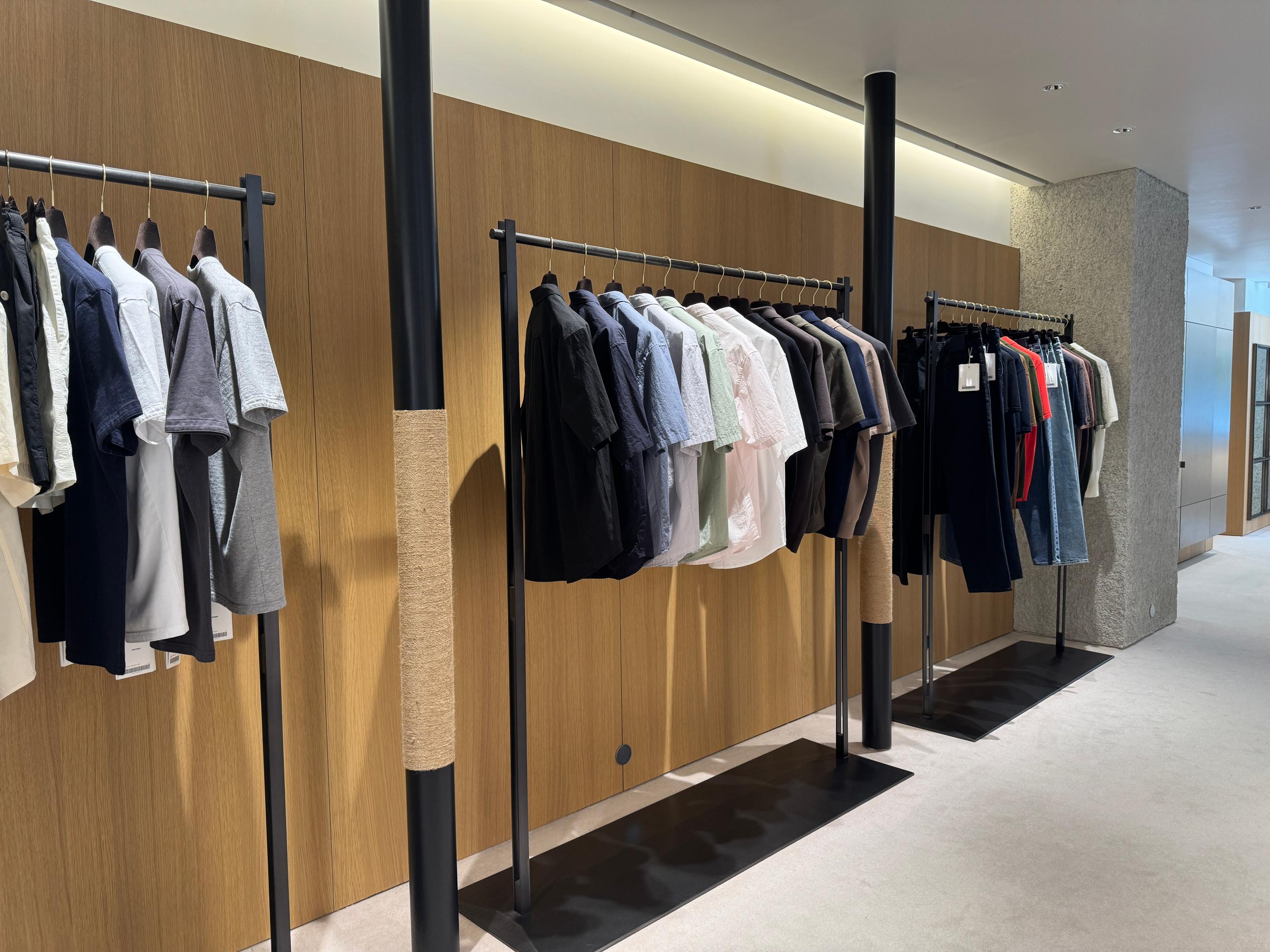 Wide shot of Pottery Seongsu store interior with stacked earth-tone knits, neutral shirts and logo caps under warm spotlighting