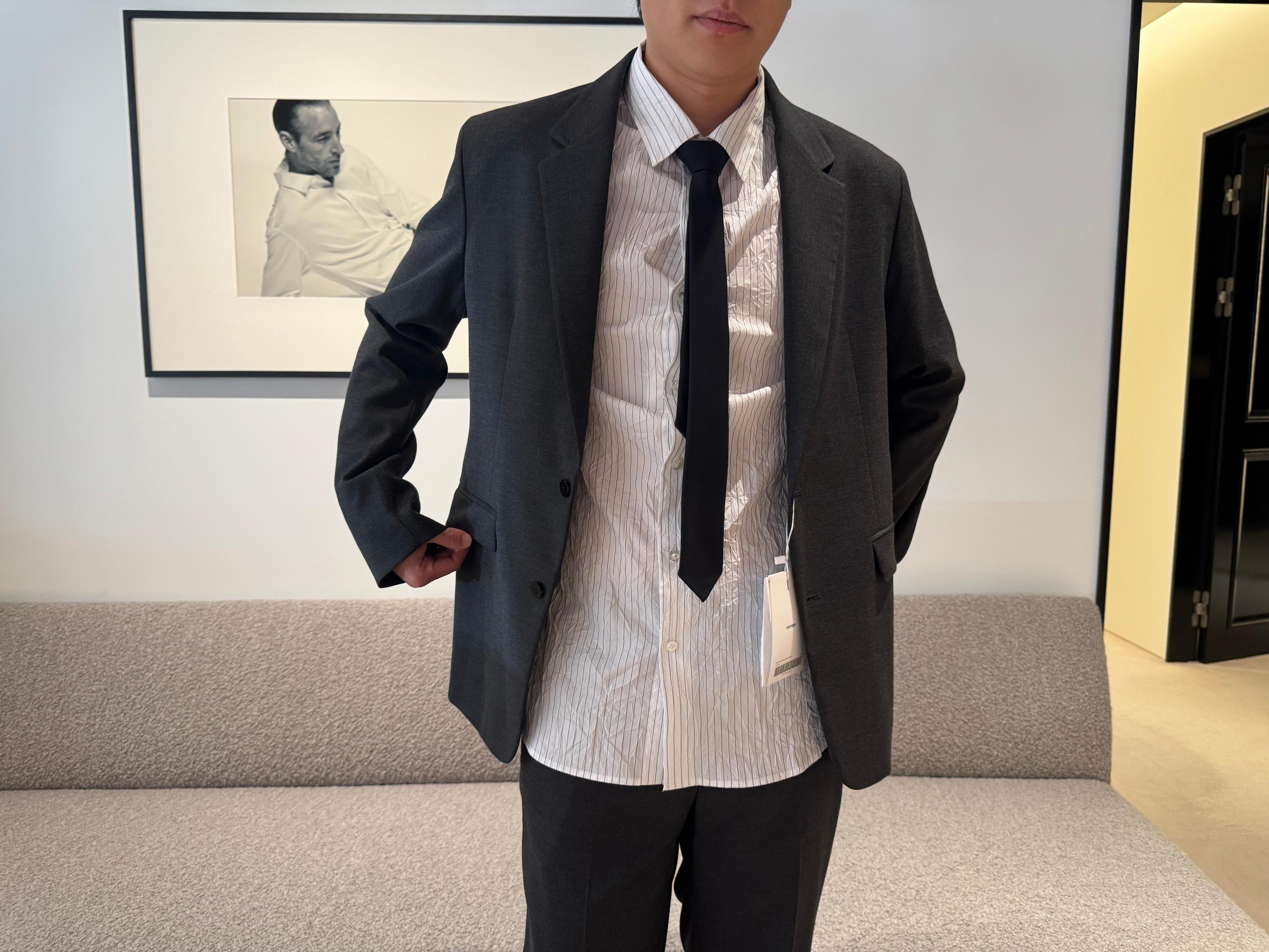 Model trying on a dark gray Pottery blazer and trousers over a white pinstripe shirt with a loose black tie, photographed inside the Seongsu store’s minimalist fitting area.