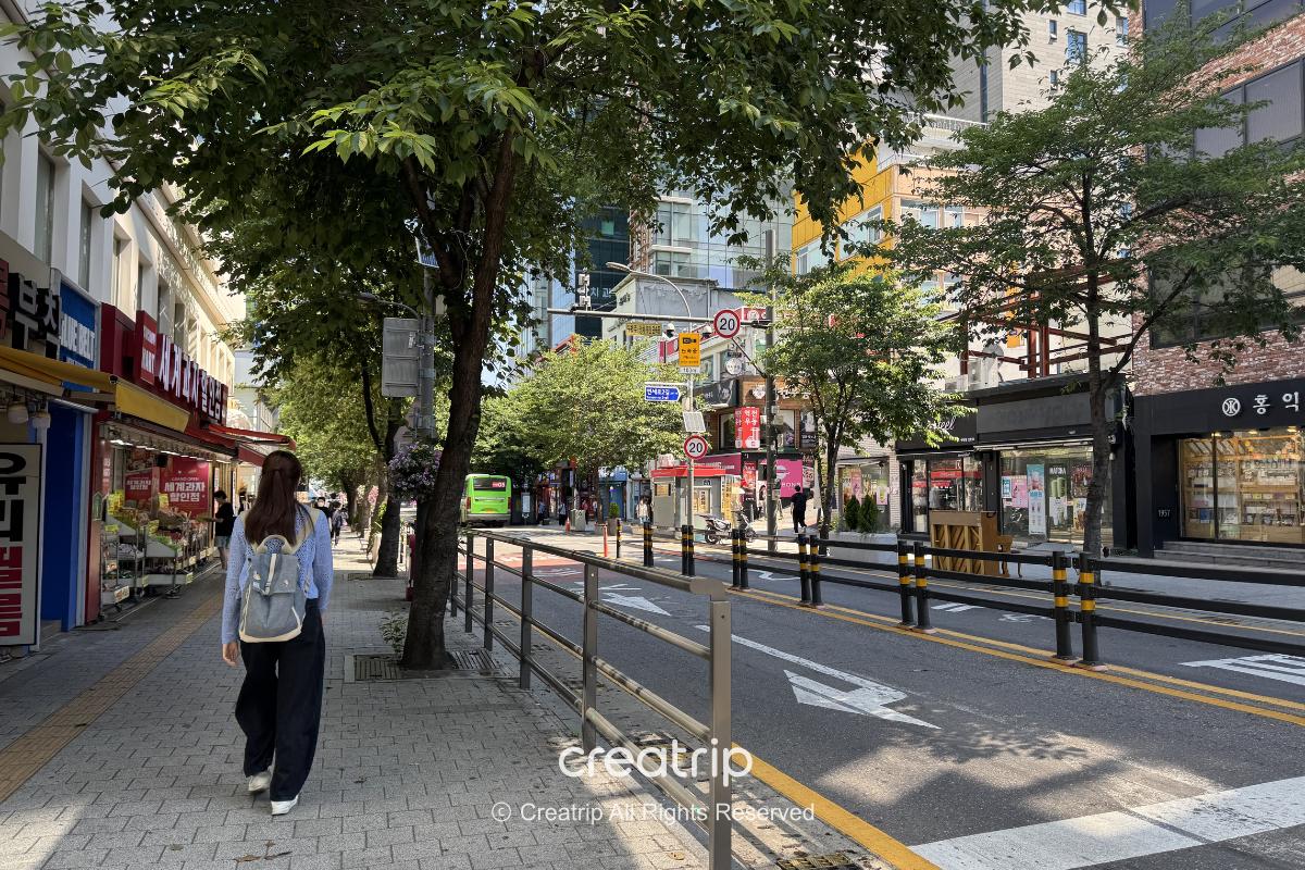 Sinchon street view, with shops on both sides, tree shade, and sidewalks